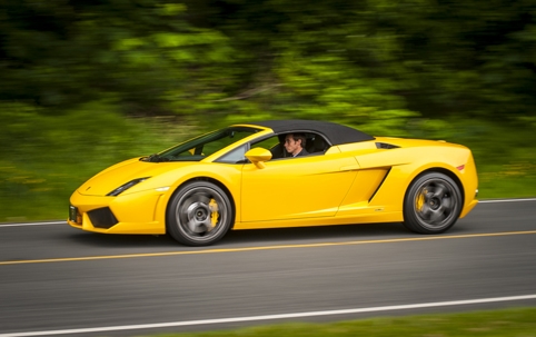 A yellow Lamborghini Gallardo is seen being driven on the road by a young male driver,
